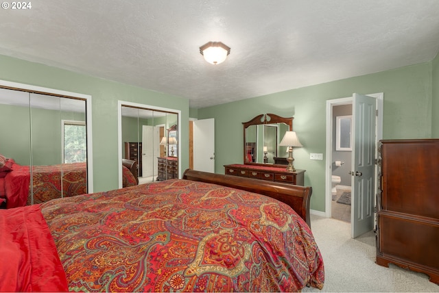 carpeted bedroom featuring two closets, ensuite bathroom, and a textured ceiling