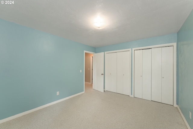 unfurnished bedroom featuring light carpet, multiple closets, and a textured ceiling