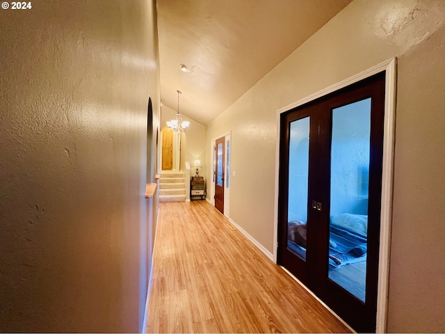 hallway with french doors, an inviting chandelier, light hardwood / wood-style flooring, and vaulted ceiling