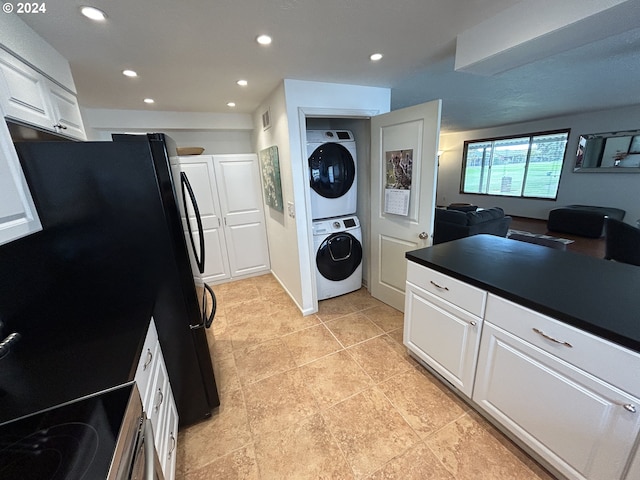 kitchen featuring black fridge, white cabinets, light tile patterned flooring, and stacked washer and clothes dryer