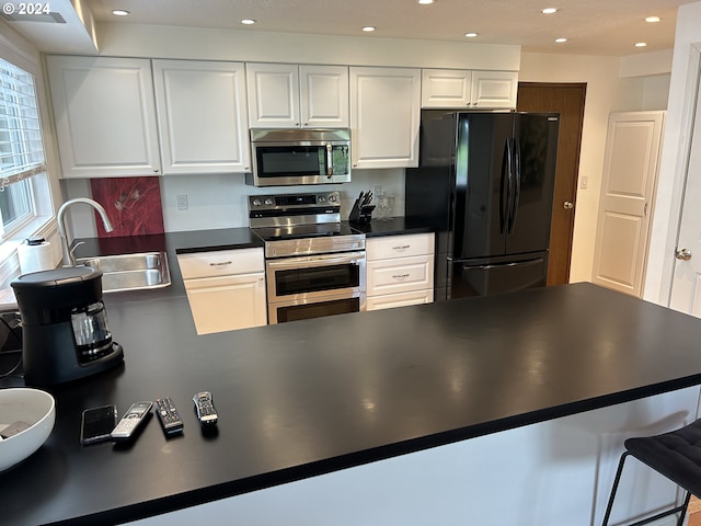 kitchen featuring white cabinets, kitchen peninsula, sink, and appliances with stainless steel finishes