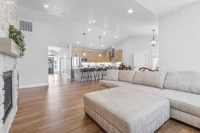 living room with a stone fireplace, high vaulted ceiling, and wood-type flooring