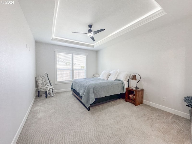 carpeted bedroom with ceiling fan, a tray ceiling, and ornamental molding