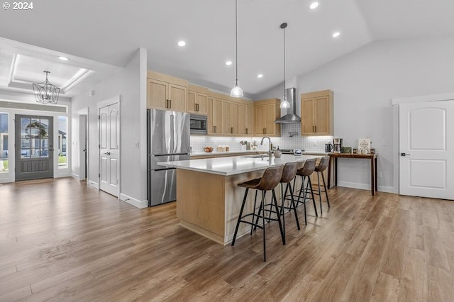 kitchen featuring wall chimney range hood, pendant lighting, backsplash, stainless steel appliances, and lofted ceiling