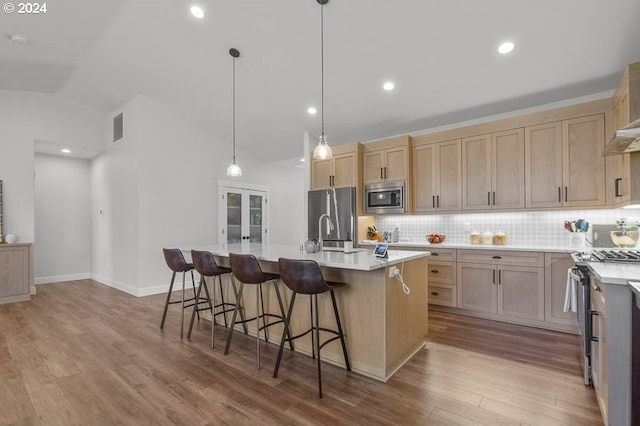 kitchen with light brown cabinets, vaulted ceiling, stainless steel appliances, and an island with sink