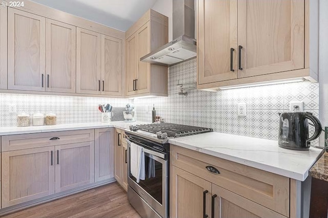 kitchen featuring light stone countertops, stainless steel gas range, decorative backsplash, wall chimney range hood, and light hardwood / wood-style flooring