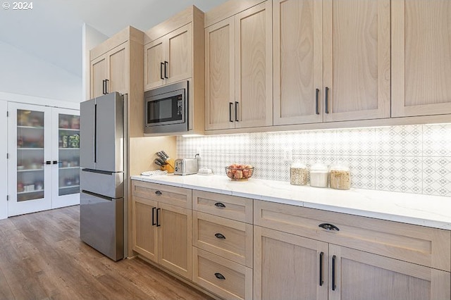 kitchen with light hardwood / wood-style flooring, light brown cabinetry, light stone counters, decorative backsplash, and stainless steel appliances