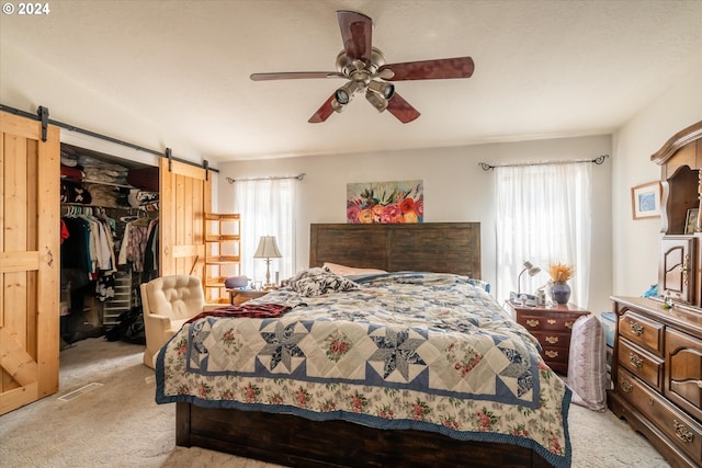 carpeted bedroom with ceiling fan, a barn door, a closet, and a spacious closet