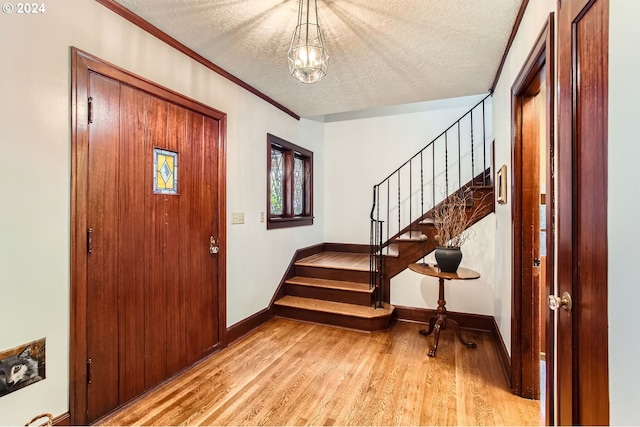 entryway with a chandelier, light hardwood / wood-style floors, a textured ceiling, and ornamental molding