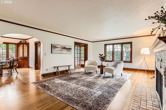 living room featuring a textured ceiling, light hardwood / wood-style floors, a brick fireplace, and ornamental molding