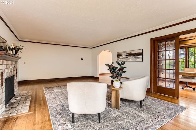 living area featuring a textured ceiling, crown molding, light wood-type flooring, and a fireplace