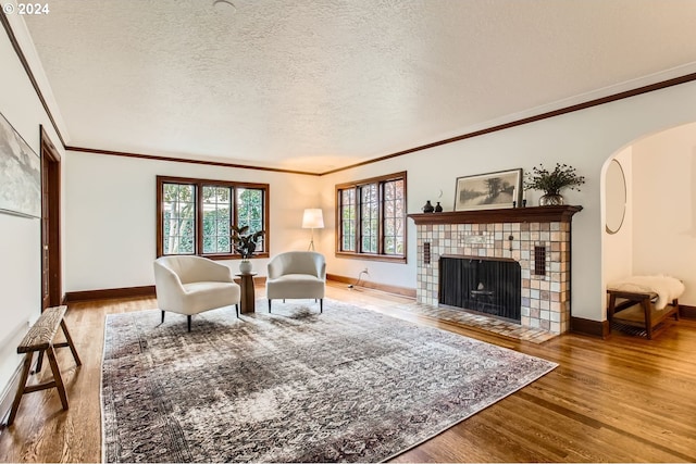 living room with a tiled fireplace, wood-type flooring, a textured ceiling, and ornamental molding