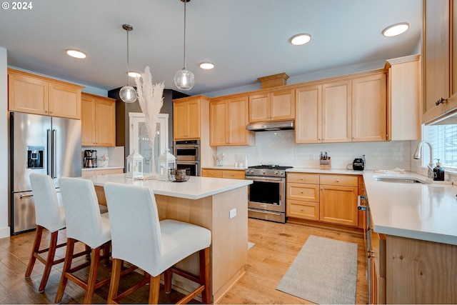 kitchen with appliances with stainless steel finishes, pendant lighting, light brown cabinetry, a kitchen island, and sink