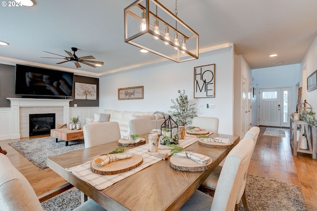 dining space featuring ceiling fan with notable chandelier, a fireplace, and hardwood / wood-style flooring