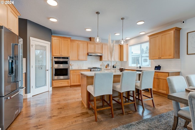 kitchen featuring pendant lighting, light brown cabinetry, a center island with sink, light hardwood / wood-style floors, and appliances with stainless steel finishes