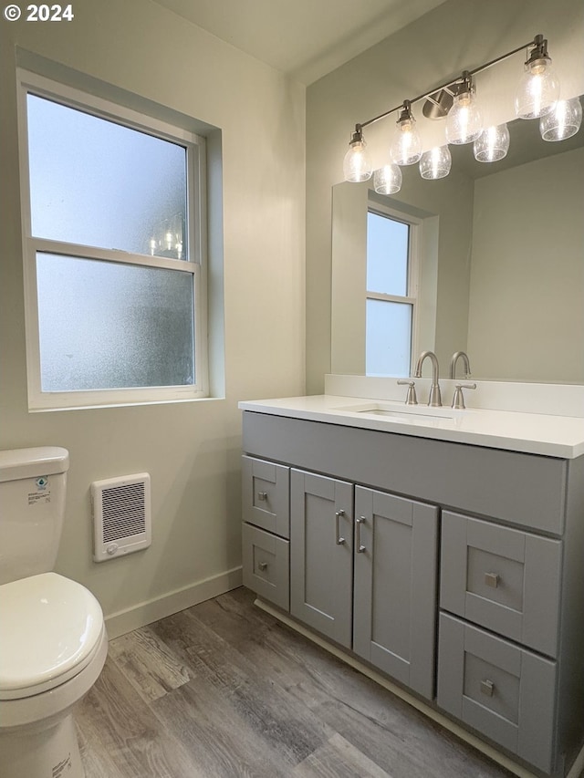 bathroom with wood-type flooring, vanity, heating unit, and toilet