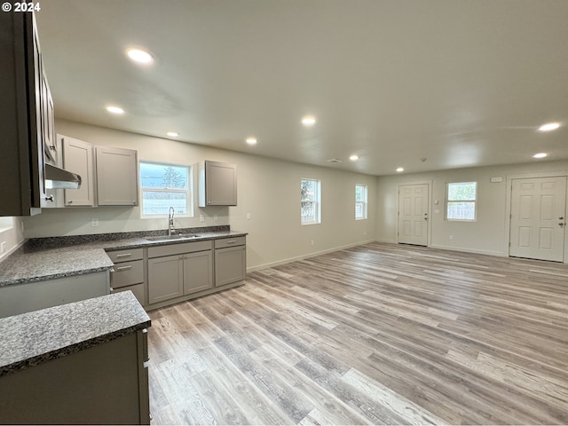 kitchen with gray cabinets, dark stone countertops, sink, and light hardwood / wood-style flooring