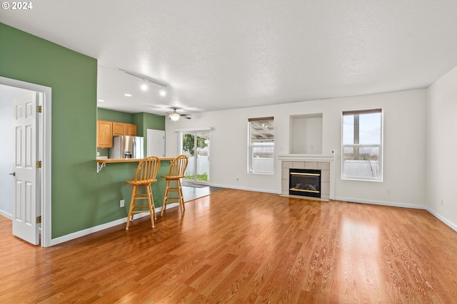 living room with ceiling fan, a textured ceiling, a tile fireplace, and light hardwood / wood-style flooring