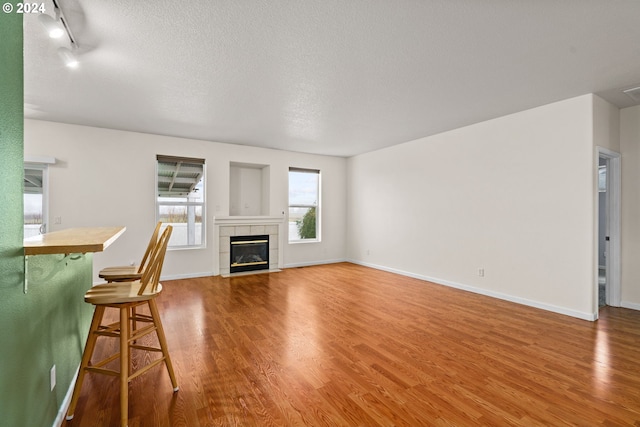 unfurnished living room with a tile fireplace, hardwood / wood-style floors, track lighting, and a textured ceiling