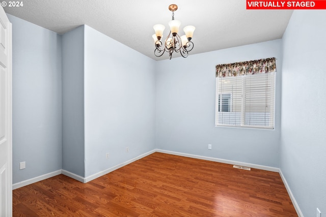 unfurnished room with a textured ceiling, hardwood / wood-style flooring, and a notable chandelier