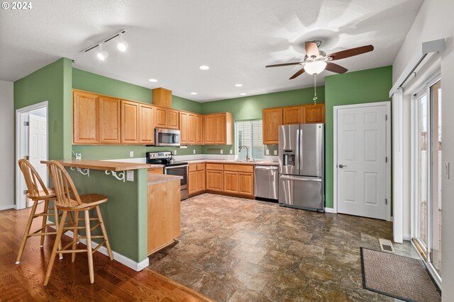 kitchen featuring kitchen peninsula, appliances with stainless steel finishes, a textured ceiling, sink, and a breakfast bar area