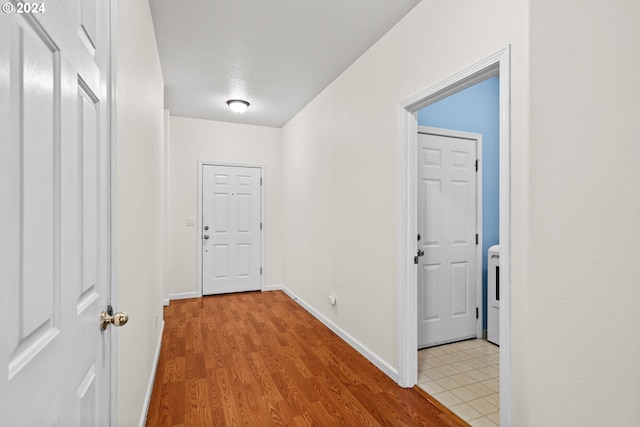 corridor with washer / dryer, a textured ceiling, and light hardwood / wood-style flooring