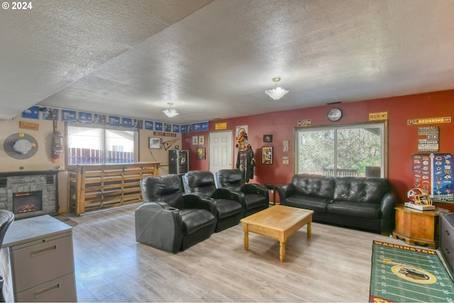 living room with a textured ceiling, a stone fireplace, and light wood-type flooring