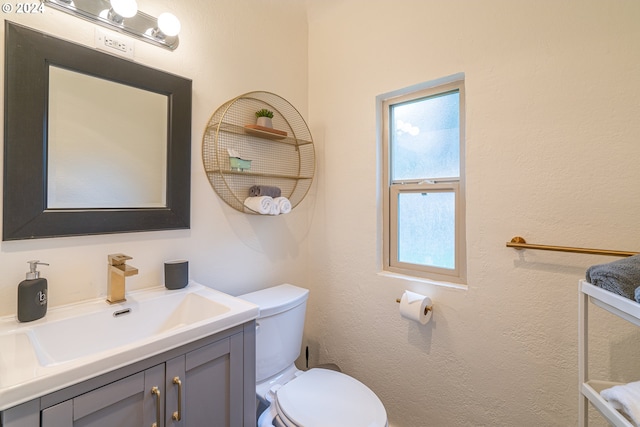 half bath with vanity, toilet, and a textured wall