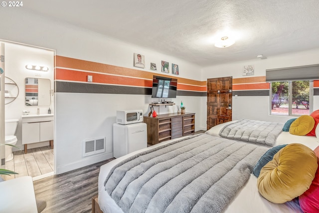 bedroom with wood finished floors, a textured ceiling, baseboards, and ensuite bath