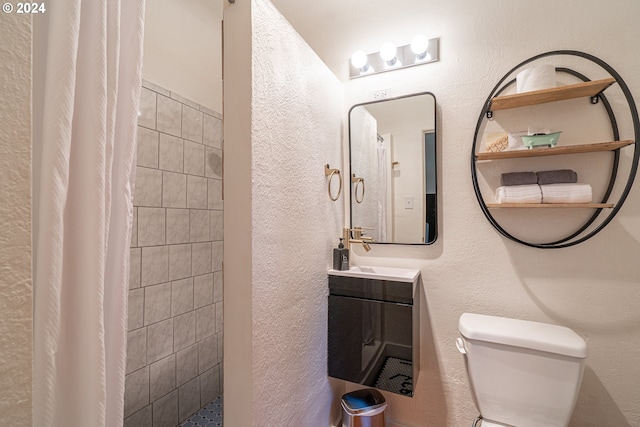 bathroom with tiled shower, a textured wall, toilet, and vanity