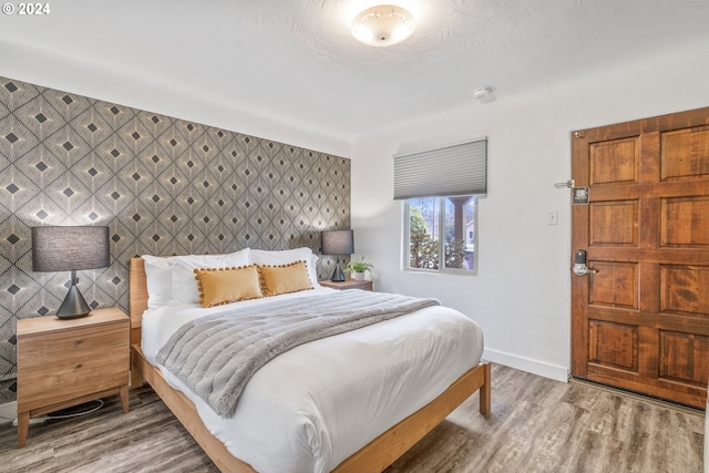 bedroom with wood finished floors, baseboards, and an accent wall