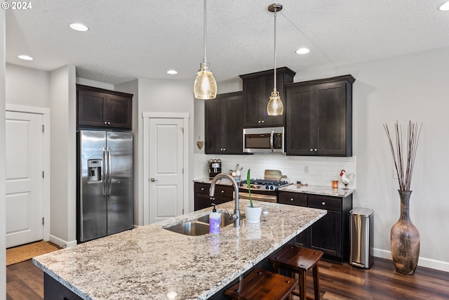 kitchen with stainless steel appliances, sink, a kitchen island with sink, and pendant lighting