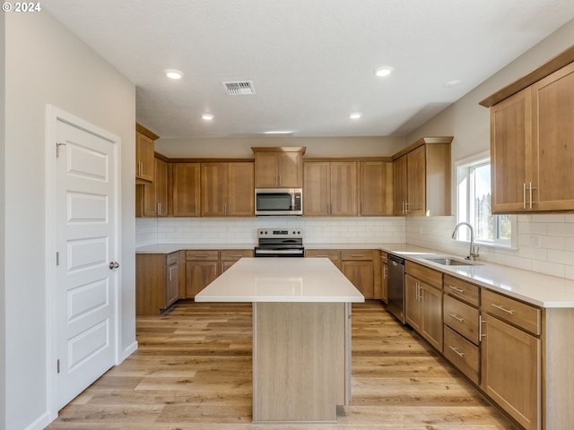 kitchen featuring light wood-type flooring, a center island, sink, decorative backsplash, and appliances with stainless steel finishes