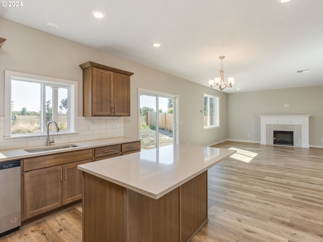 kitchen with dishwasher, light hardwood / wood-style floors, a tile fireplace, sink, and an inviting chandelier