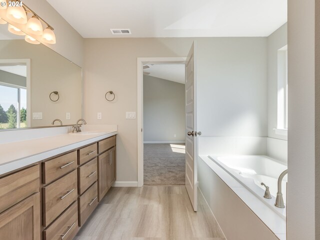 bathroom with a bathtub, vanity, vaulted ceiling, and hardwood / wood-style flooring