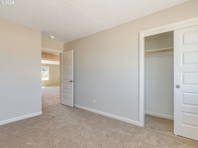 unfurnished bedroom with light colored carpet, a textured ceiling, and a closet