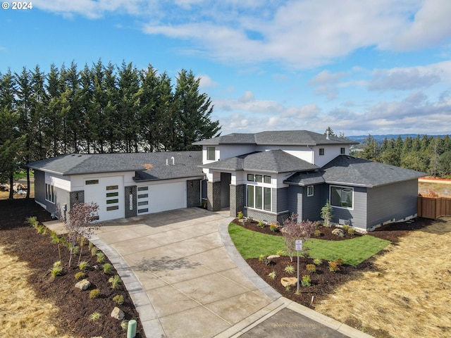 prairie-style home featuring concrete driveway, a shingled roof, a garage, and a front yard