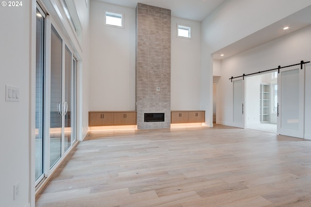 unfurnished living room featuring light hardwood / wood-style flooring, a high ceiling, a tile fireplace, and a barn door