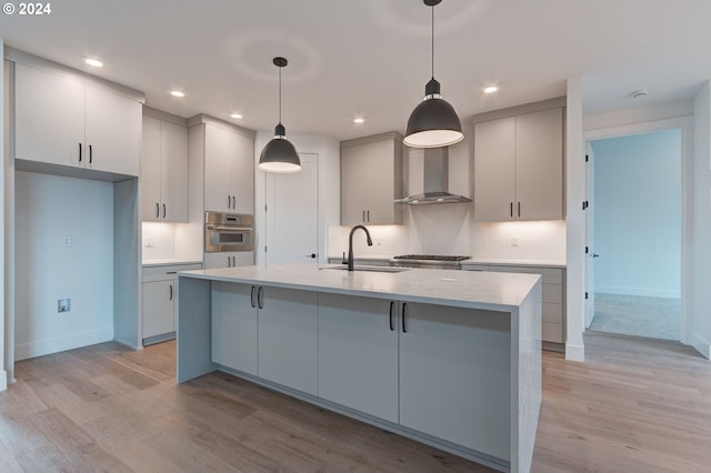 kitchen with an island with sink, stainless steel oven, sink, light hardwood / wood-style floors, and decorative light fixtures