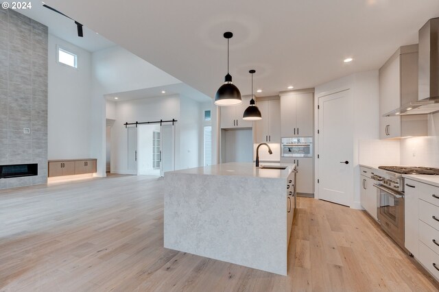 kitchen featuring hanging light fixtures, appliances with stainless steel finishes, a barn door, wall chimney exhaust hood, and sink