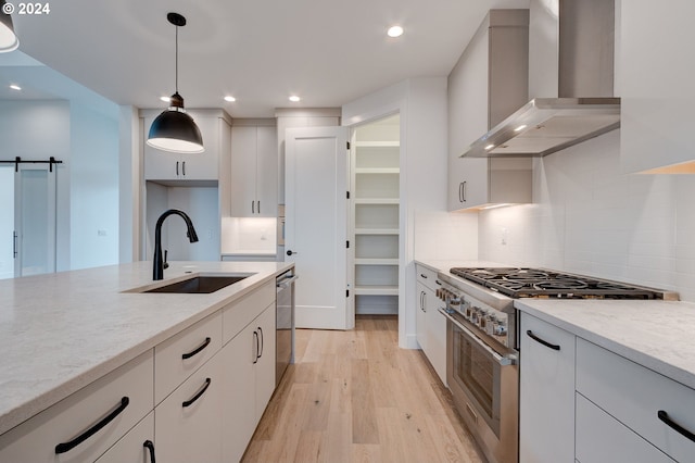 kitchen with wall chimney range hood, sink, appliances with stainless steel finishes, a barn door, and white cabinetry