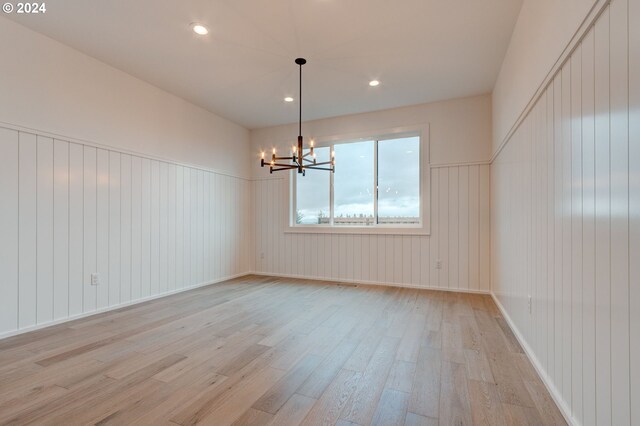 unfurnished dining area featuring wood walls, a chandelier, and light wood-type flooring