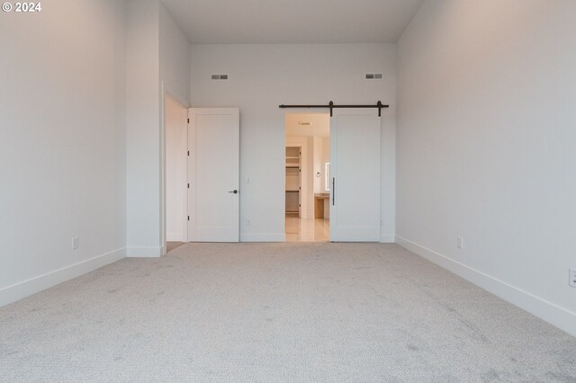 unfurnished bedroom featuring a closet, a spacious closet, carpet floors, and a barn door