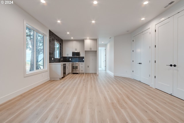 kitchen featuring light wood-type flooring, a sink, backsplash, recessed lighting, and appliances with stainless steel finishes