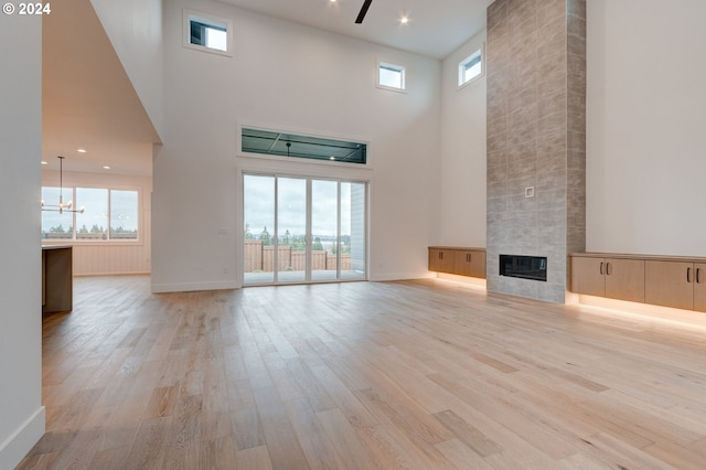 unfurnished living room with a towering ceiling, a fireplace, light wood-type flooring, and ceiling fan