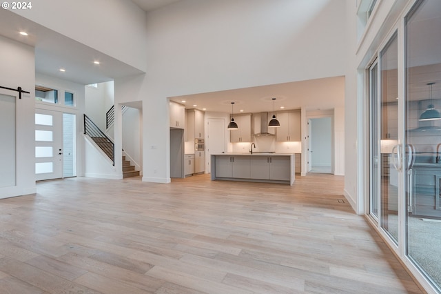 unfurnished living room with light wood-style flooring, baseboards, a towering ceiling, and stairs