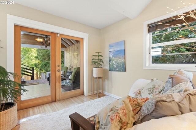 living area featuring french doors, lofted ceiling with beams, a notable chandelier, and light wood-type flooring