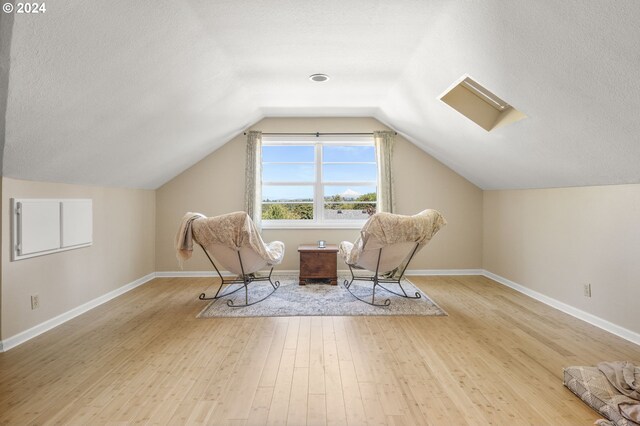 unfurnished room featuring hardwood / wood-style floors, a textured ceiling, and vaulted ceiling