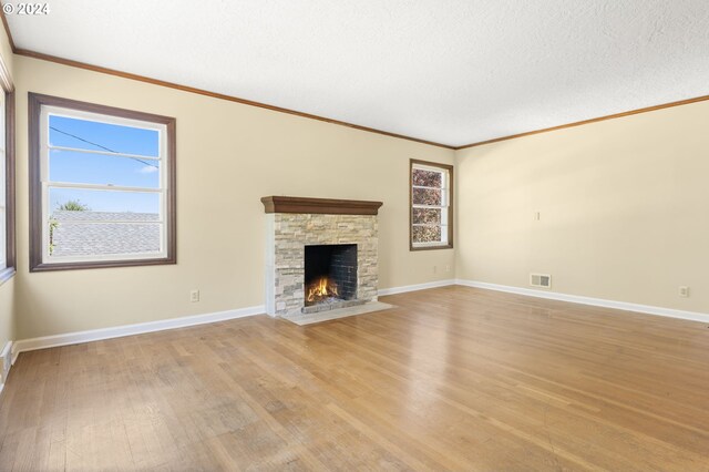 unfurnished living room featuring light hardwood / wood-style floors, a stone fireplace, ornamental molding, and a textured ceiling