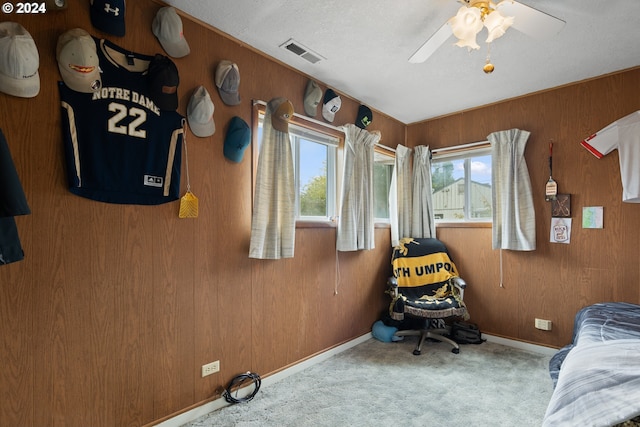 carpeted bedroom with ceiling fan, wooden walls, and a textured ceiling